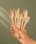 Hand holding a set of wooden cutlery against a green background
