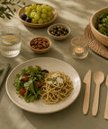 Dining table setting with pasta, salad, and wooden cutlery on a green tablecloth.