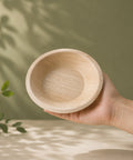 Hand holding a small wooden bowl against a natural background with greenery.