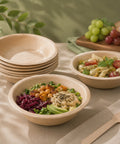 Bamboo bowls with salad and pasta on a table with grapes and bread.