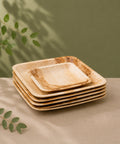 Stack of square wooden plates on a neutral surface with greenery in the background